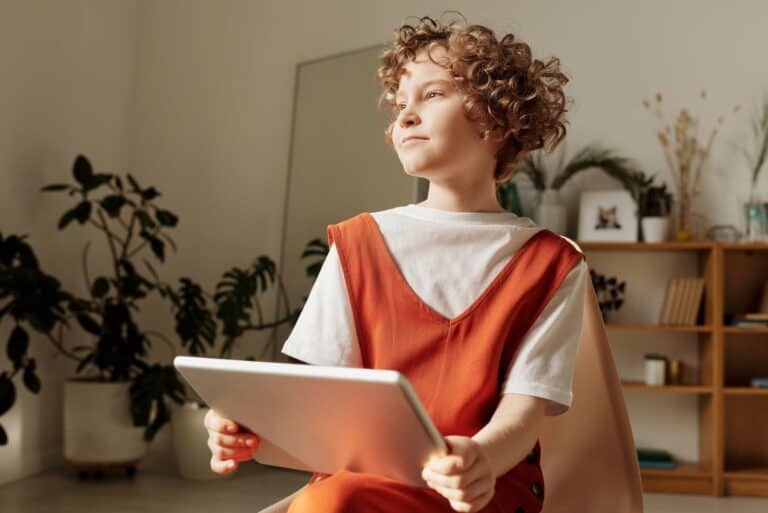 Photo of Child Sitting on Chair While Holding Tablet